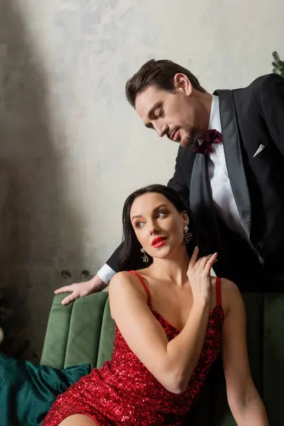 Beau monsieur en smoking regardant belle femme en robe rouge assis sur le canapé, couple riche — Photo de stock