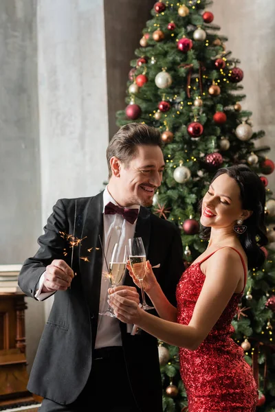 Bel homme riche en tenue formelle tenant verre de champagne près décoré arbre de Noël — Photo de stock