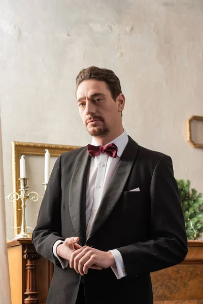 Cavalheiro rico em traje formal com gravata borboleta em pé perto de piano na véspera de Natal, férias — Fotografia de Stock