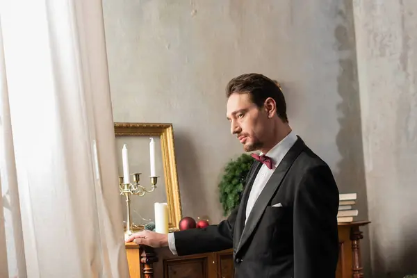 Elegante gentiluomo in abito formale con papillon in piedi vicino al pianoforte la vigilia di Natale, vacanza — Foto stock