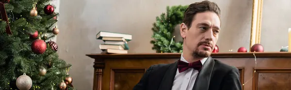 Елегантний джентльмен в смокінгу з краваткою, що сидить біля фортепіано і прикрашена ялинка, банер — стокове фото