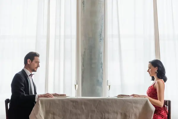 Beau couple en robe de soirée assis à la table à manger avec des verres de champagne, mode de vie riche — Photo de stock