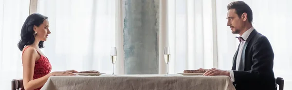 Beautiful couple in evening gown sitting at dining table with champagne glasses, wealthy banner — Stock Photo