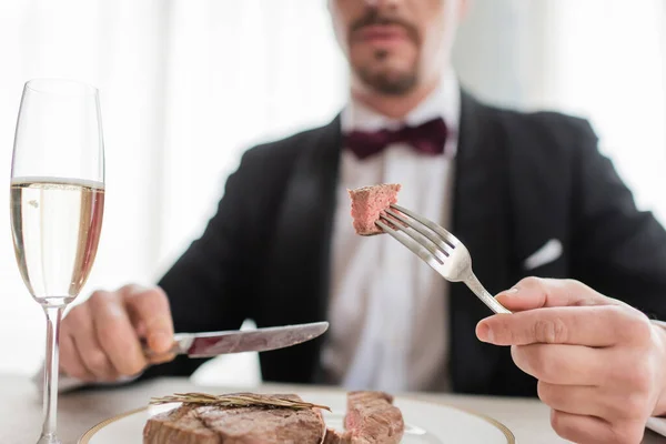 Cropped view of wealthy gentleman in tuxedo holding cutlery with tasty cooked beef steak, close up — Stock Photo
