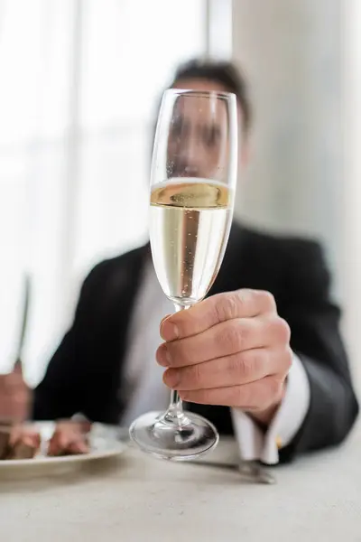 Обрезанный вид джентльмена в костюме, держащего бокал шампанского за ужином, крупным планом — стоковое фото