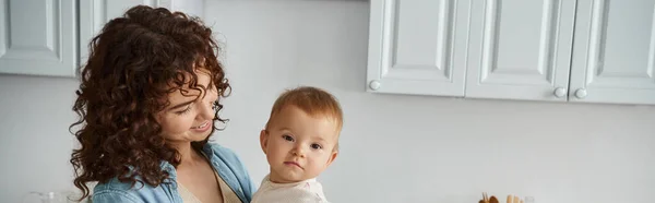 Adorabile bambina che guarda la macchina fotografica vicino sorridente madre in cucina a casa, banner orizzontale — Foto stock
