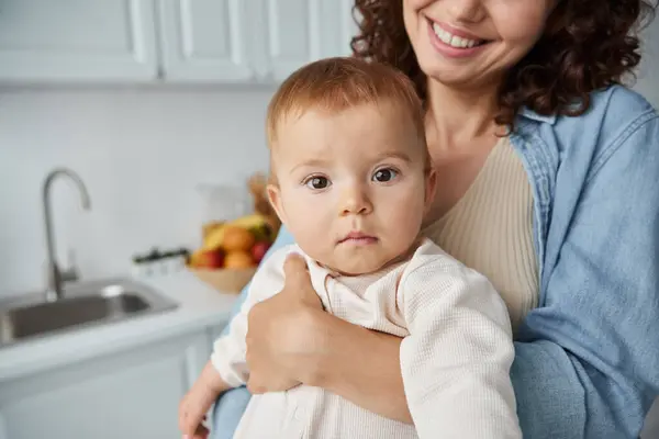 Retrato de niña adorable en manos de madre alegre en la cocina en casa, infancia feliz - foto de stock