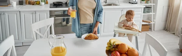 Niño jugando con pinzas de madera cerca de mamá con delicioso croissant y jugo de naranja fresco, pancarta — Stock Photo