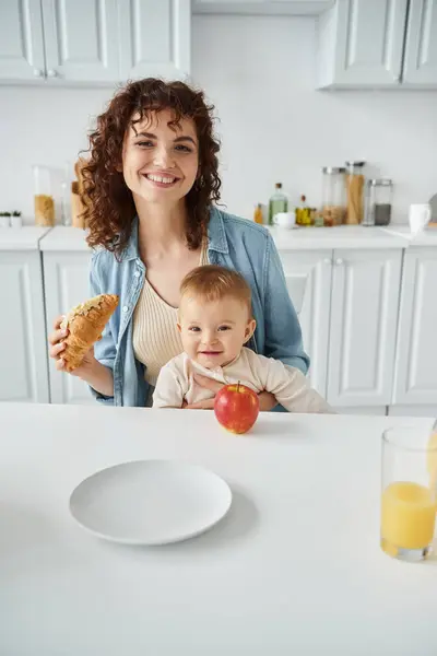 Madre e hijo pequeño sonriendo cerca de croissant y jugo de naranja fresco con manzana durante el desayuno — Stock Photo