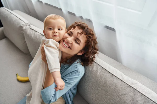 Overjoyed woman with closed eyes holding adorable toddler daughter on couch in living room — Stock Photo