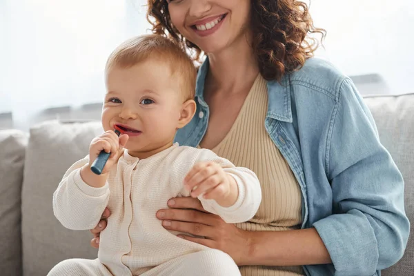 Little girl chewing teething toy near smiling happy on couch in living room, happy childhood — Stock Photo