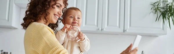 Smiley-Frau hält Kleinkind-Tochter mit Babyflasche und macht Selfie auf Handy, Banner — Stockfoto