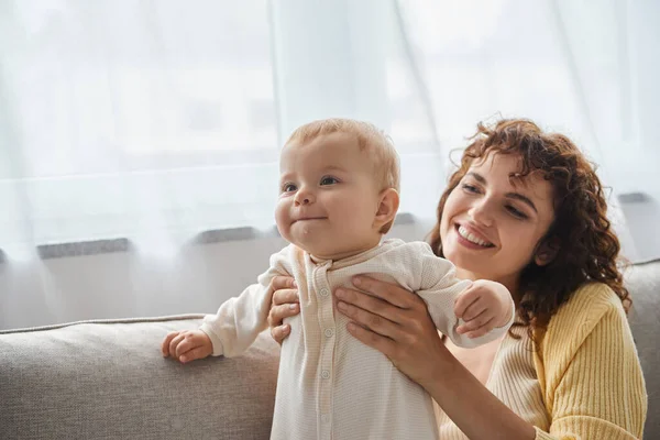 Vida familiar feliz, mulher sorridente segurando adorável bebê menina no sofá na sala de estar em casa — Fotografia de Stock