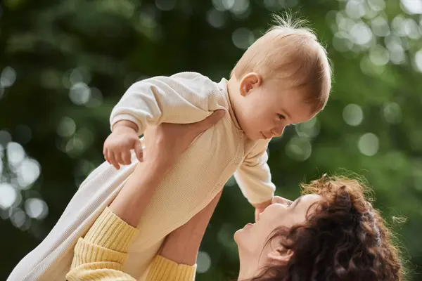 Glückliche Frau, die mit ihrer kleinen Tochter spielt und sie in den Händen im Freien aufzieht, glückselige Mutterschaft — Stockfoto