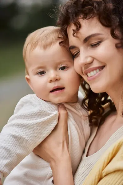 Porträt einer lächelnden Frau mit geschlossenen Augen, die ihr Kleinkind im Freien umarmt, glückliche Momente — Stockfoto