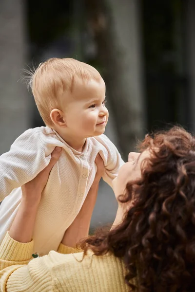 Frau mit welligem Haar hält kleine Tochter im Strampler, während sie Zeit im Freien verbringt — Stockfoto