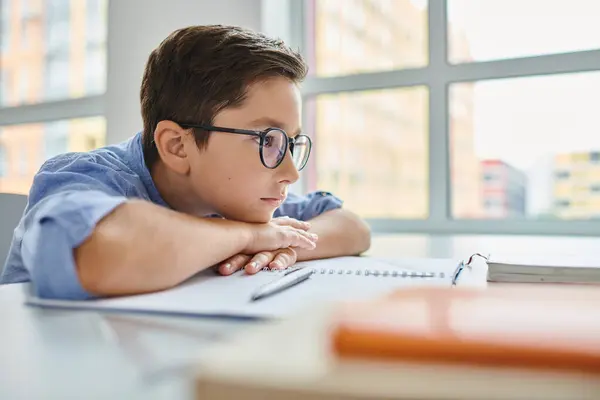 Сосредоточенный мальчик в очках, внимательно сидящий за столом, погруженный в учебу или работу над заданием. — стоковое фото