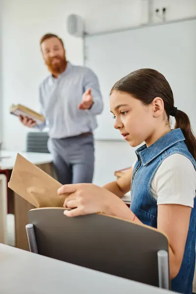Girl is reading book while listening to male teacher — Stock Photo