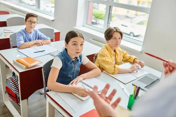 Group of children attentively listening to a man teacher as they sit at desks in a bright, lively classroom setting. — Stock Photo