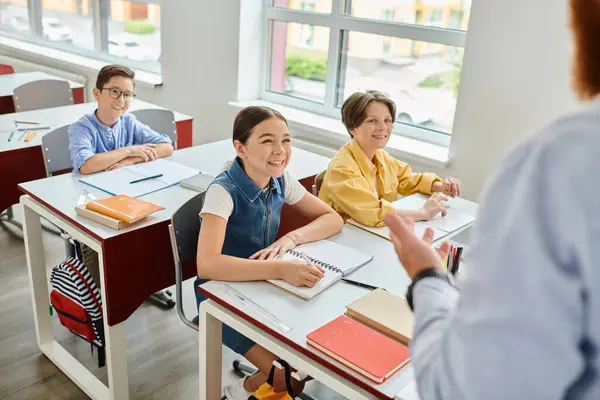 Una vivace scena in classe in cui un insegnante di sesso maschile sta fornendo istruzioni a un gruppo di bambini seduti alle scrivanie. — Foto stock