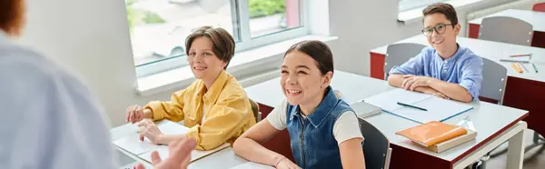 A man teacher instructs a group of kids sitting at desks in a bright, lively classroom setting. — Stock Photo