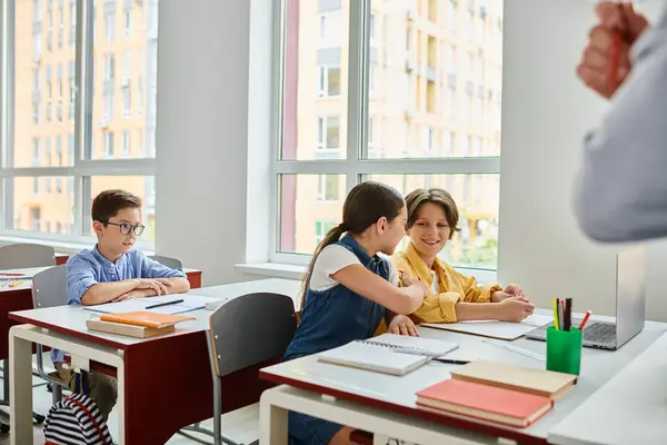 A group of children sit at desks in a bright classroom, focusing on a man teacher giving instructions. — Stock Photo