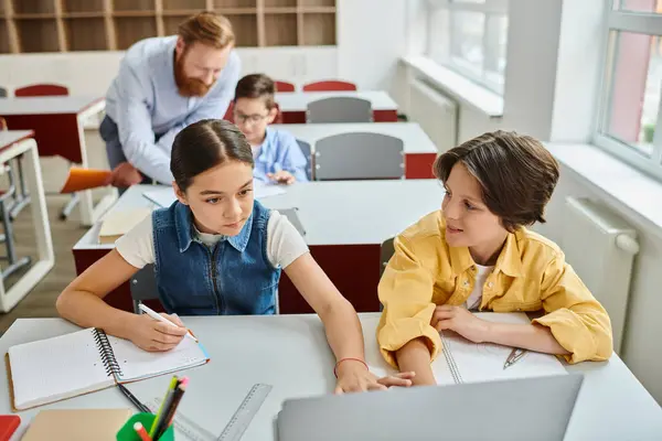 Un gruppo di bambini siede alla scrivania in una classe luminosa, ascoltando attentamente un insegnante che li istruisce.. — Foto stock