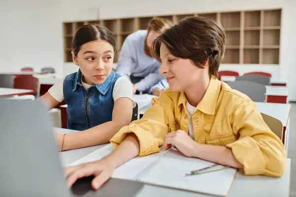 Un ragazzo e una ragazza si impegnano con attenzione a un tavolo con un computer portatile, assorbiti in un'esperienza di apprendimento condivisa — Foto stock