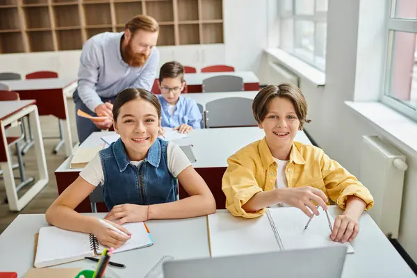 Un gruppo di bambini si siede attentamente alle scrivanie, ascoltando le istruzioni di un insegnante di sesso maschile in un'aula luminosa e vivace. — Foto stock