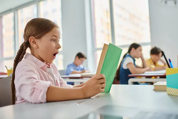 Una joven inmersa en un libro, absorbiendo conocimientos, se sienta en un salón de clases animado - foto de stock