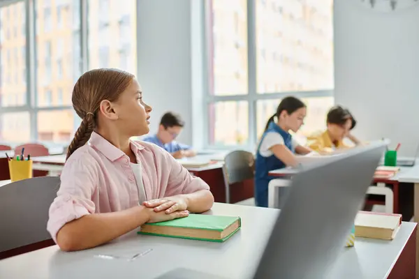 Uma menina imersa em seu trabalho, senta-se em uma mesa com um laptop aberto na frente dela, focada e envolvida no mundo digital. — Fotografia de Stock