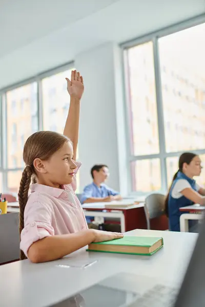 Молода дівчина з довгим волоссям піднімає руку в барвистому, жвавому класі. — стокове фото