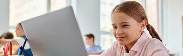 Una giovane ragazza, seduta di fronte a un computer portatile in una luminosa aula, è impegnata ad esplorare il mondo virtuale — Foto stock