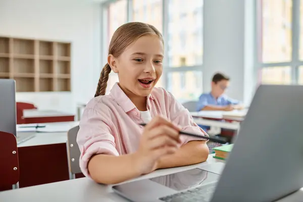 Uma jovem senta-se atentamente na frente de um computador portátil, absorvido em suas atividades on-line em um ambiente de sala de aula brilhante. — Fotografia de Stock