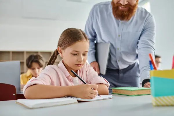 Un uomo premuroso guida una bambina attraverso i suoi compiti in un'aula luminosa e vivace piena di studenti — Foto stock