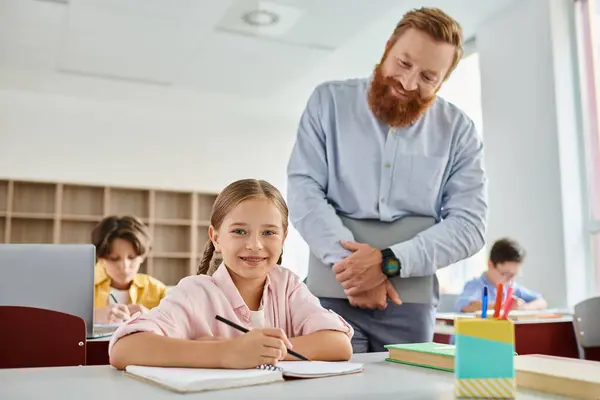 A man teacher in a classroom standing beside a little girl, both engaged in learning and teaching. — Stock Photo