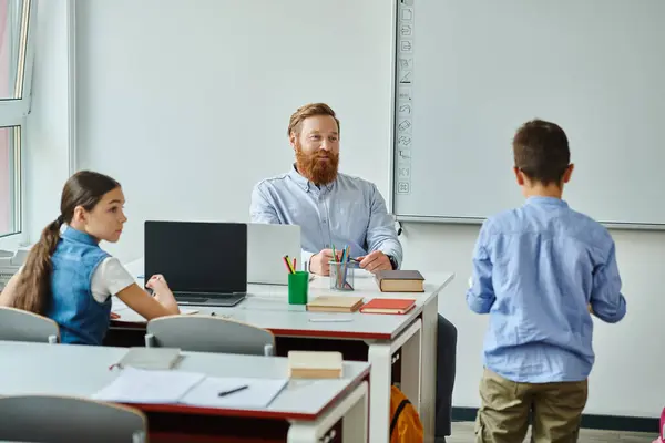 A man sits at a desk in front of a group of children, engaging them in a lively classroom setting. — Stock Photo