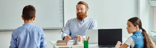 A group of kids are attentively listening to their male teacher as they sit around a colorful table in a bright and lively classroom. — Stock Photo