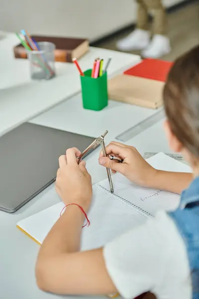 Un niño se sienta en una mesa, sosteniendo la brújula de dibujo en las manos - foto de stock