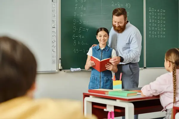 Un uomo in piedi accanto a una bambina davanti a una lavagna, che insegna in una classe luminosa e vivace. — Foto stock