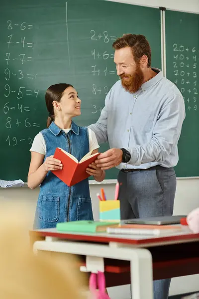 Un homme se tient à côté d'une petite fille devant un tableau noir, engageant une conversation éducative animée dans une salle de classe lumineuse. — Photo de stock