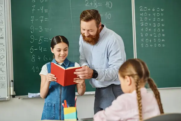 Un insegnante di sesso maschile condivide un libro con una giovane ragazza in una classe colorata piena di studenti che ascoltano con entusiasmo la storia. — Foto stock