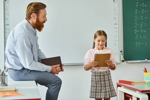 A man, possibly a teacher, sits on a chair next to a little girl, engaging in a moment of mentorship or guidance. — Stock Photo