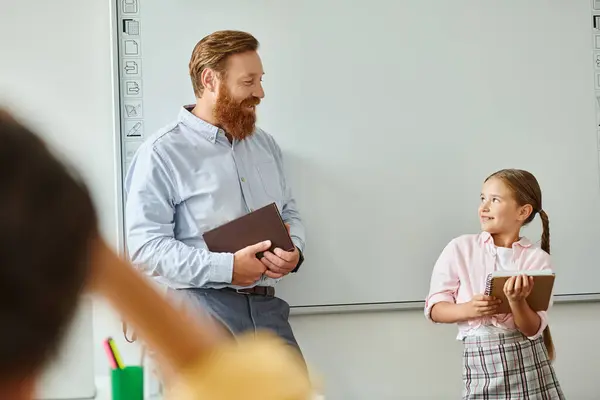 Un uomo sta accanto a una bambina davanti a una lavagna bianca in una classe luminosa, impegnandosi in un apprendimento interattivo.. — Foto stock