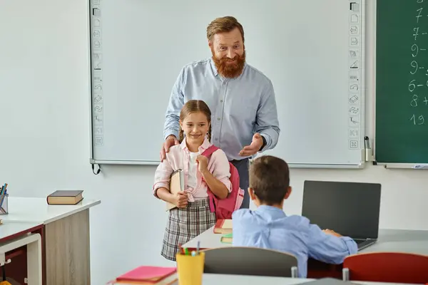 Un homme enseignant debout à côté d'une petite fille dans une salle de classe dynamique, discutant et s'engageant dans des activités éducatives avec un groupe d'enfants. — Photo de stock