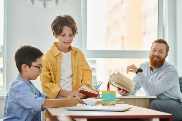 Un grupo de niños sentados en una mesa, absortos en libros mientras un maestro masculino conduce una animada discusión. - foto de stock