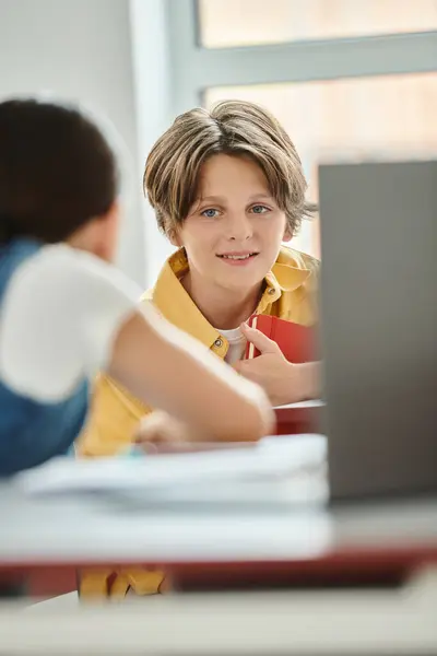 Un ragazzo si siede ad una scrivania in una classe vibrante, immerso nello schermo del suo portatile — Foto stock
