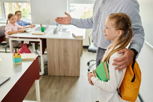 A man, a teacher, stands beside a little girl in a lively office setting, offering guidance and support. — Stock Photo