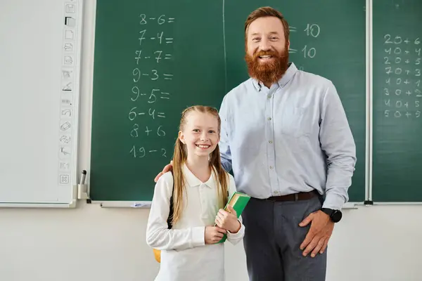 Un uomo si trova accanto a una bambina davanti a una lavagna, impegnato in una vivace sessione di apprendimento in un ambiente luminoso in classe. — Foto stock