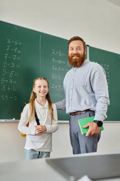 Un uomo si trova accanto a una bambina davanti a una lavagna in una vibrante classe, insegnandola e guidandola in un vivace ambiente educativo.. — Foto stock